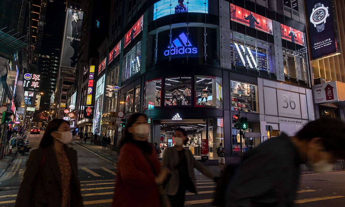 Pedestrians wearing face masks walk past the Adidas store and logo