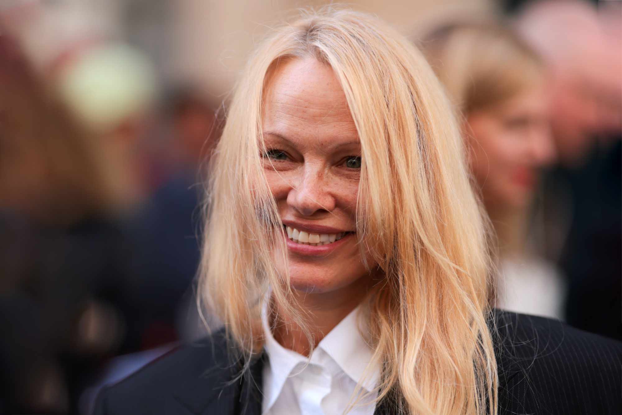 Pam Anderson wears a grey blazer and white shirt at The Row's FW24 fashion show in Paris
