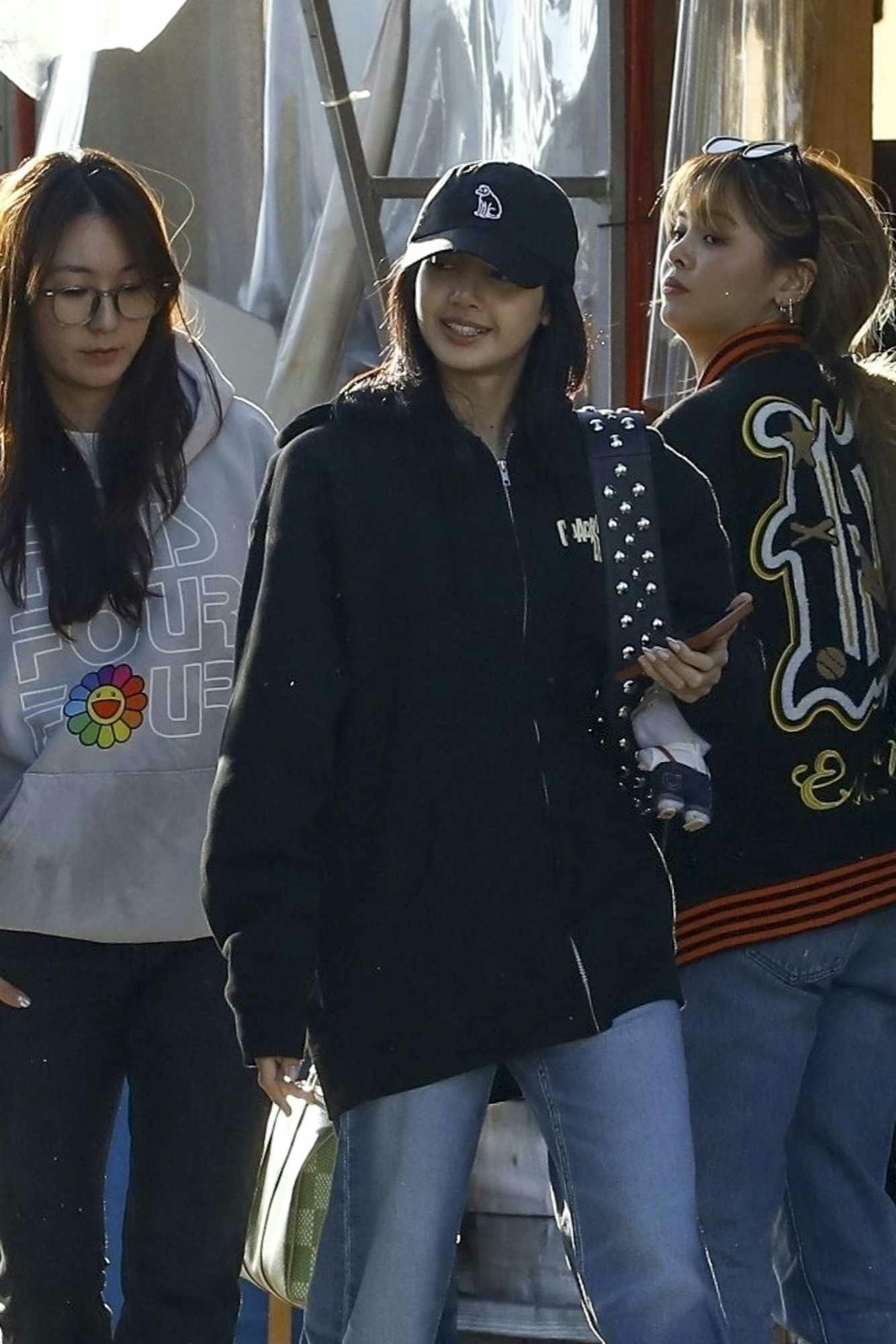 Lisa from BLACKPINK wears a black cap, Coachella 2024 hoodie, blue jeans, and white sneakers in beverly hills