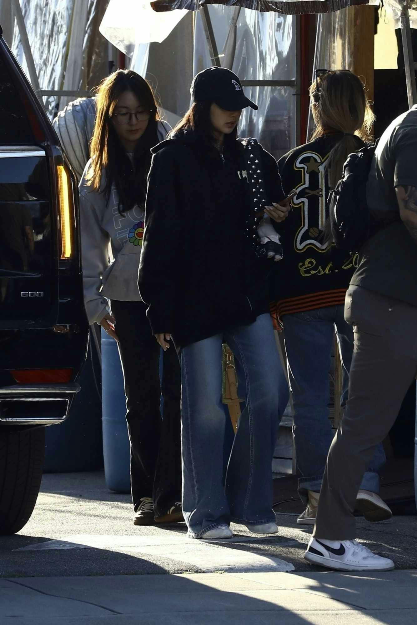 Lisa from BLACKPINK wears a black cap, Coachella 2024 hoodie, blue jeans, and white sneakers in beverly hills