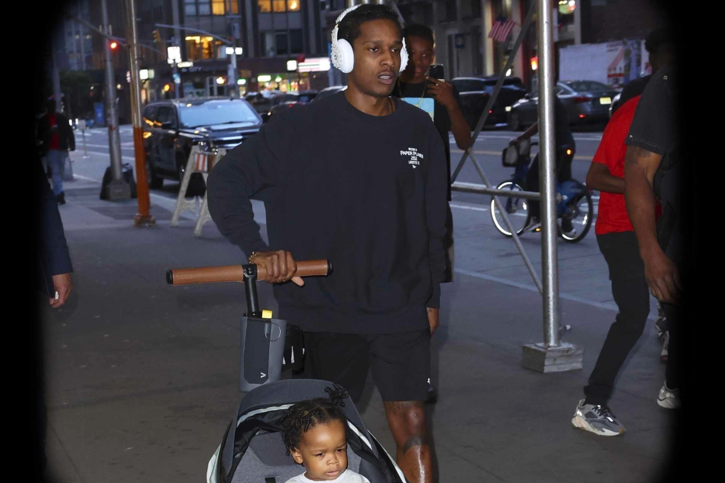 A$AP Rocky wears a black sweater, black shorts, Puma sneakers and pearl-studded Beats headphones while walking with kids RZA & Riot Rose