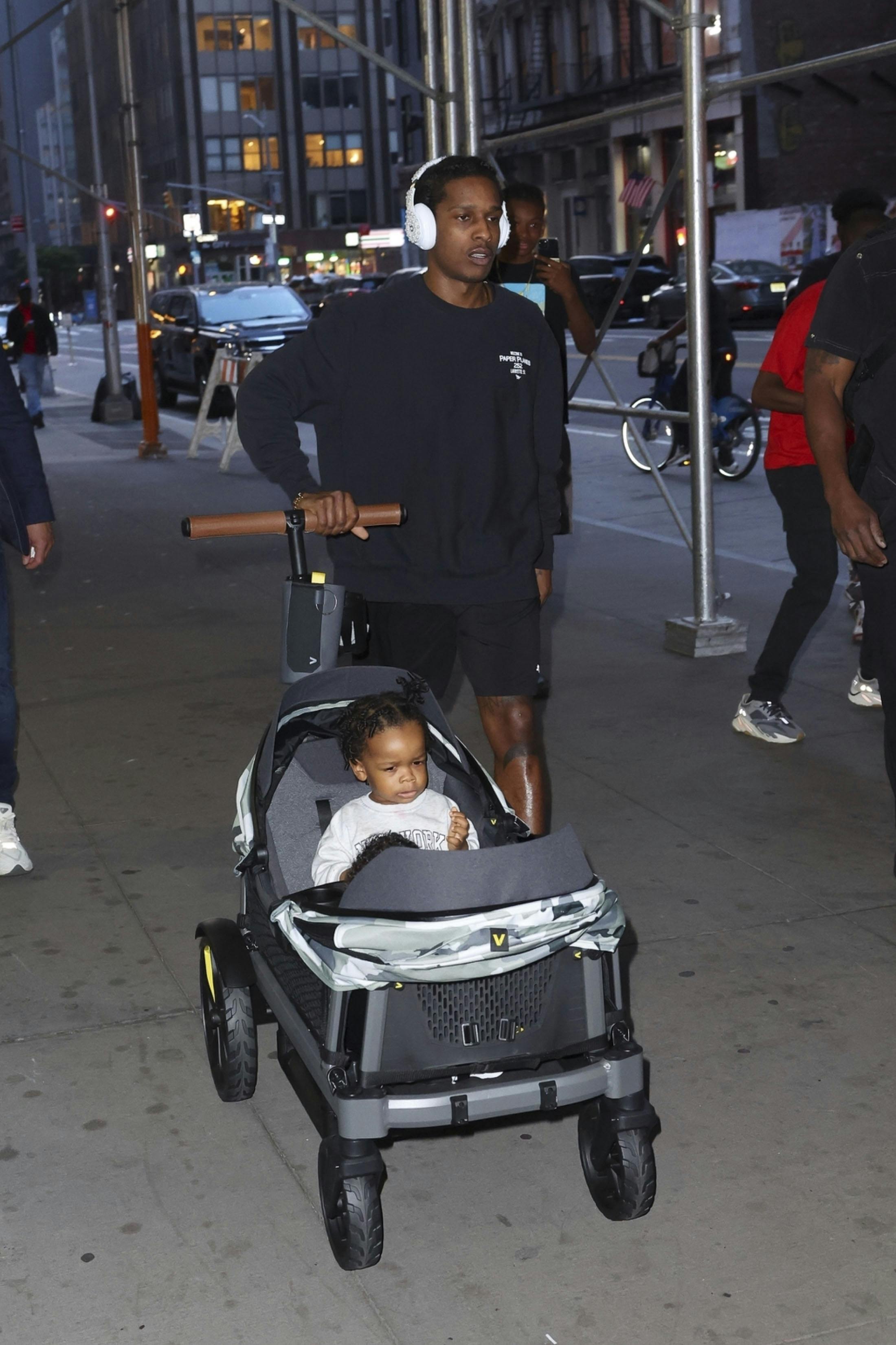 A$AP Rocky wears a black sweater, black shorts, Puma sneakers and pearl-studded Beats headphones while walking with kids RZA & Riot Rose