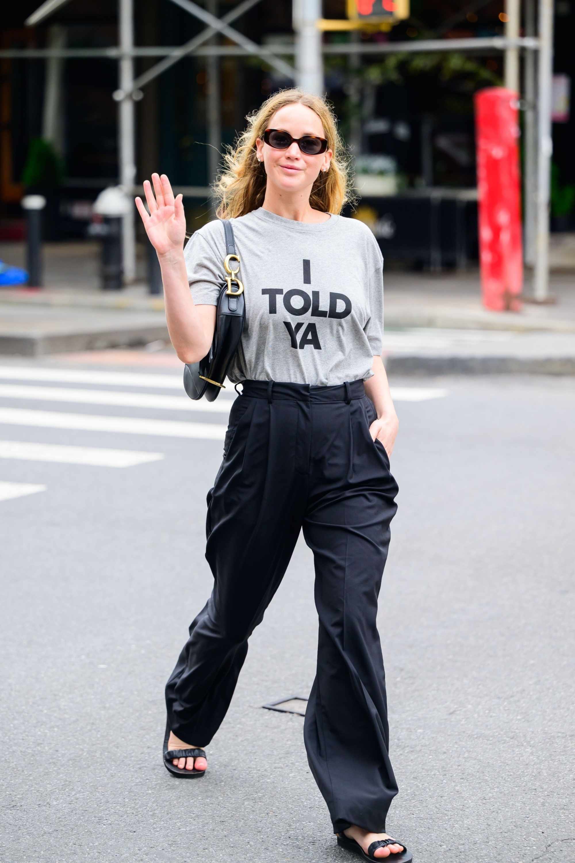 Jennifer Lawrence wears an I Told Ya T-shirt, black pant, sunglasses & a Dior Saddle bag