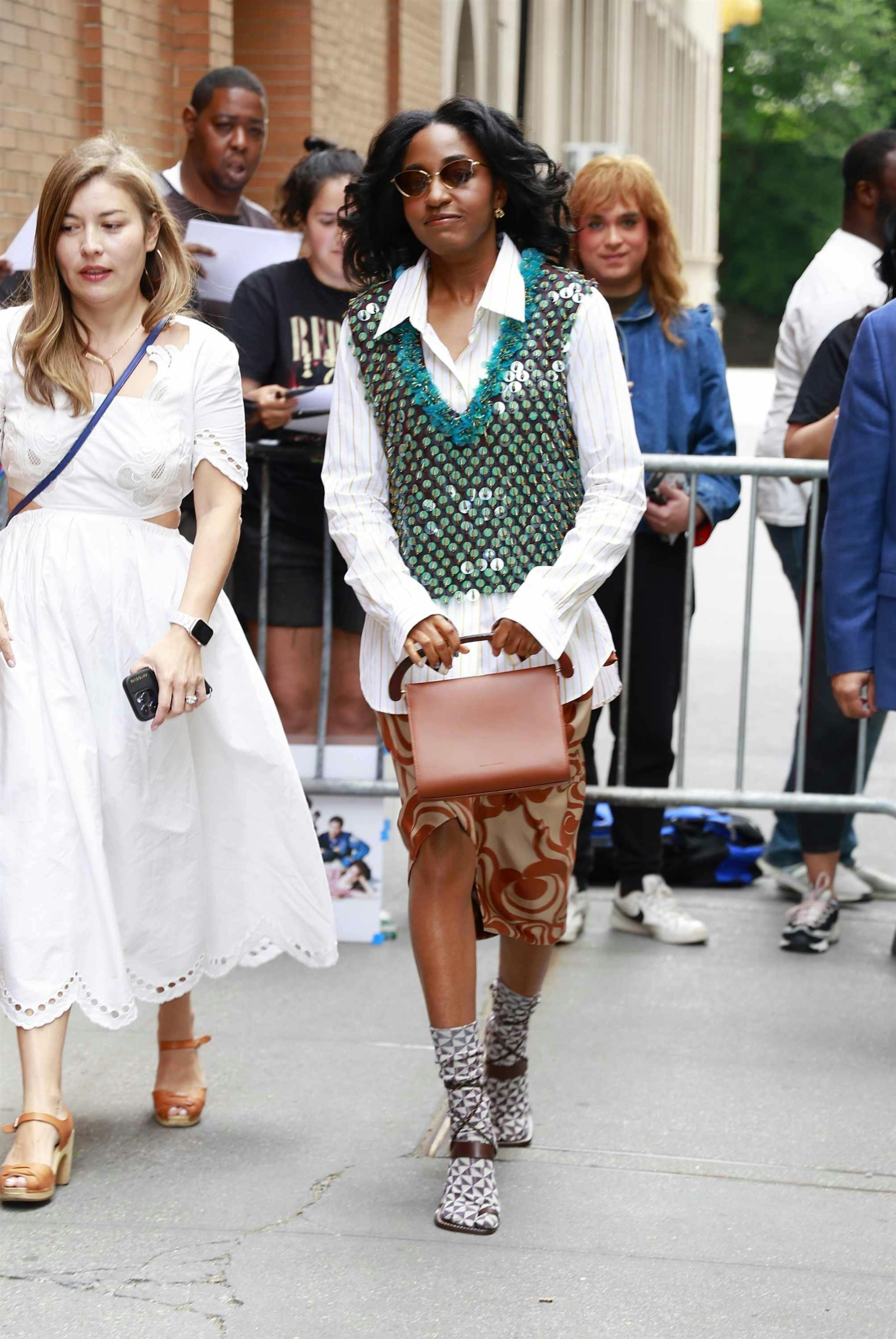 Ayo Edebiri wearing a gold vest, striped shirt, patterned skirt, and socks with heels