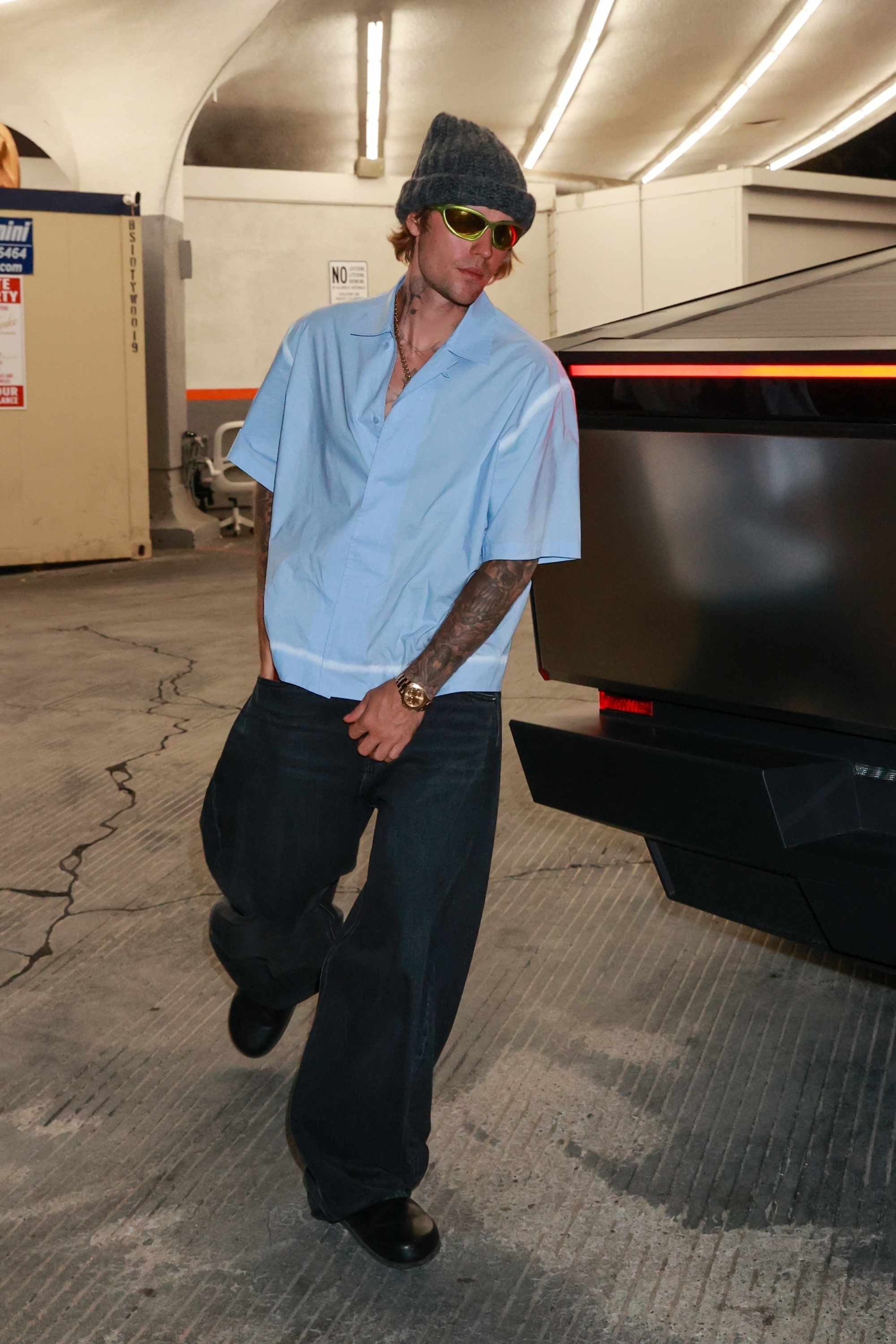 Justin Bieber wears grey beanie, technical sunglasses, baggy Balenciaga jeans & black clogs with Hailey Bieber in a black dress & sunglasses