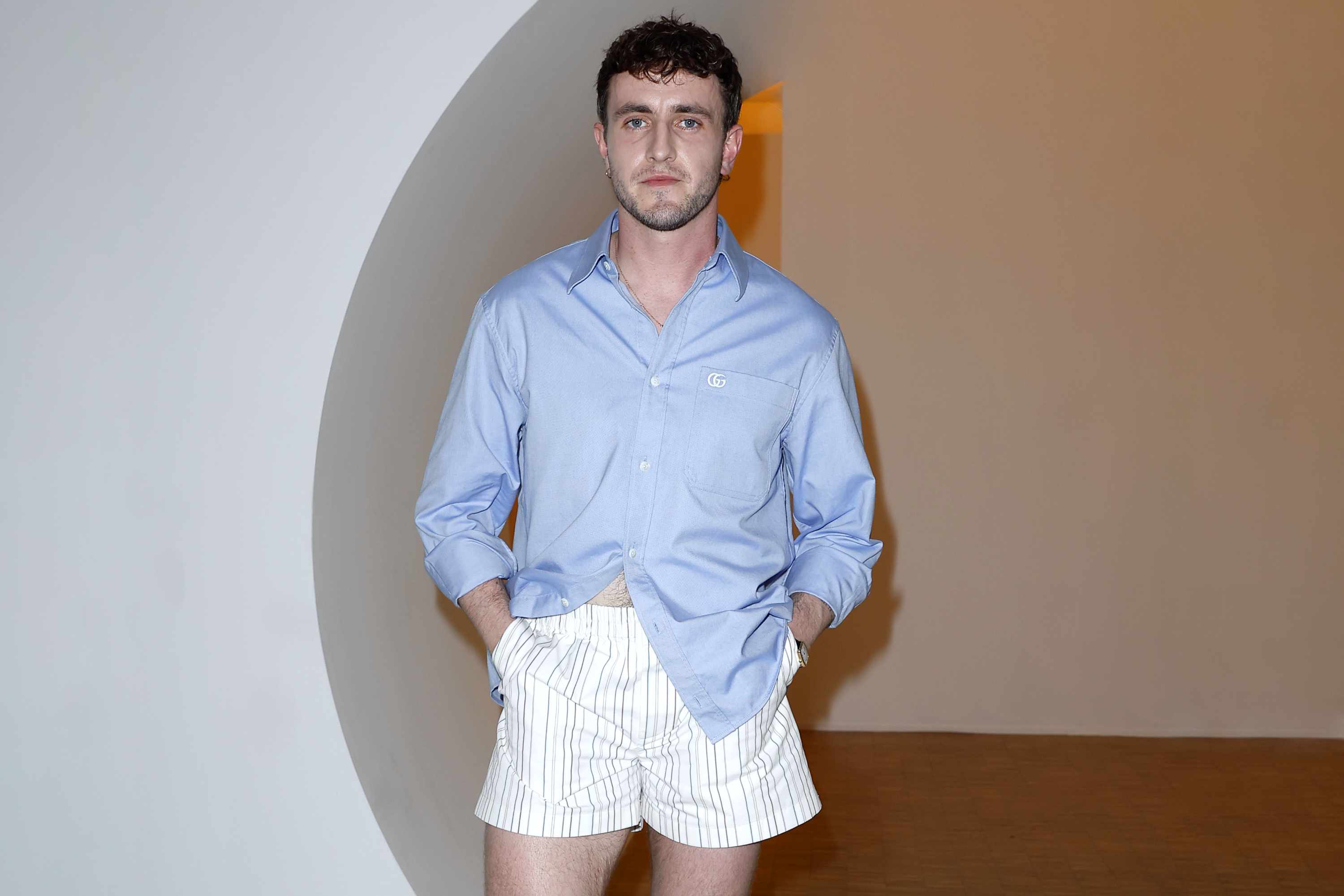 Paul Mescal wears a blue Gucci shirt tucked into short striped shorts and white socks with black shoes at the June 17 Gucci menswear show in Milan