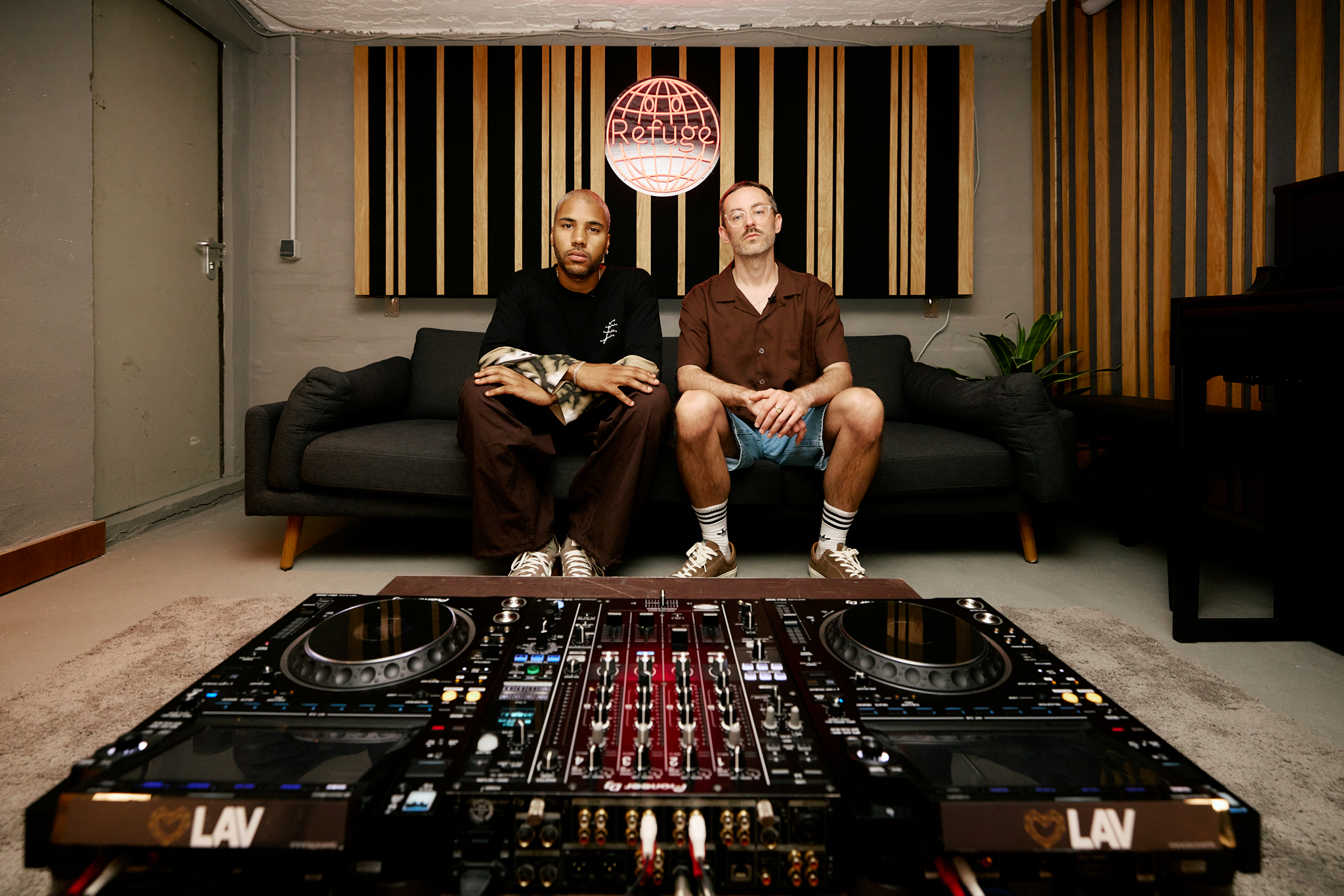 The founders of a radio station sitting on a sofa behind decks