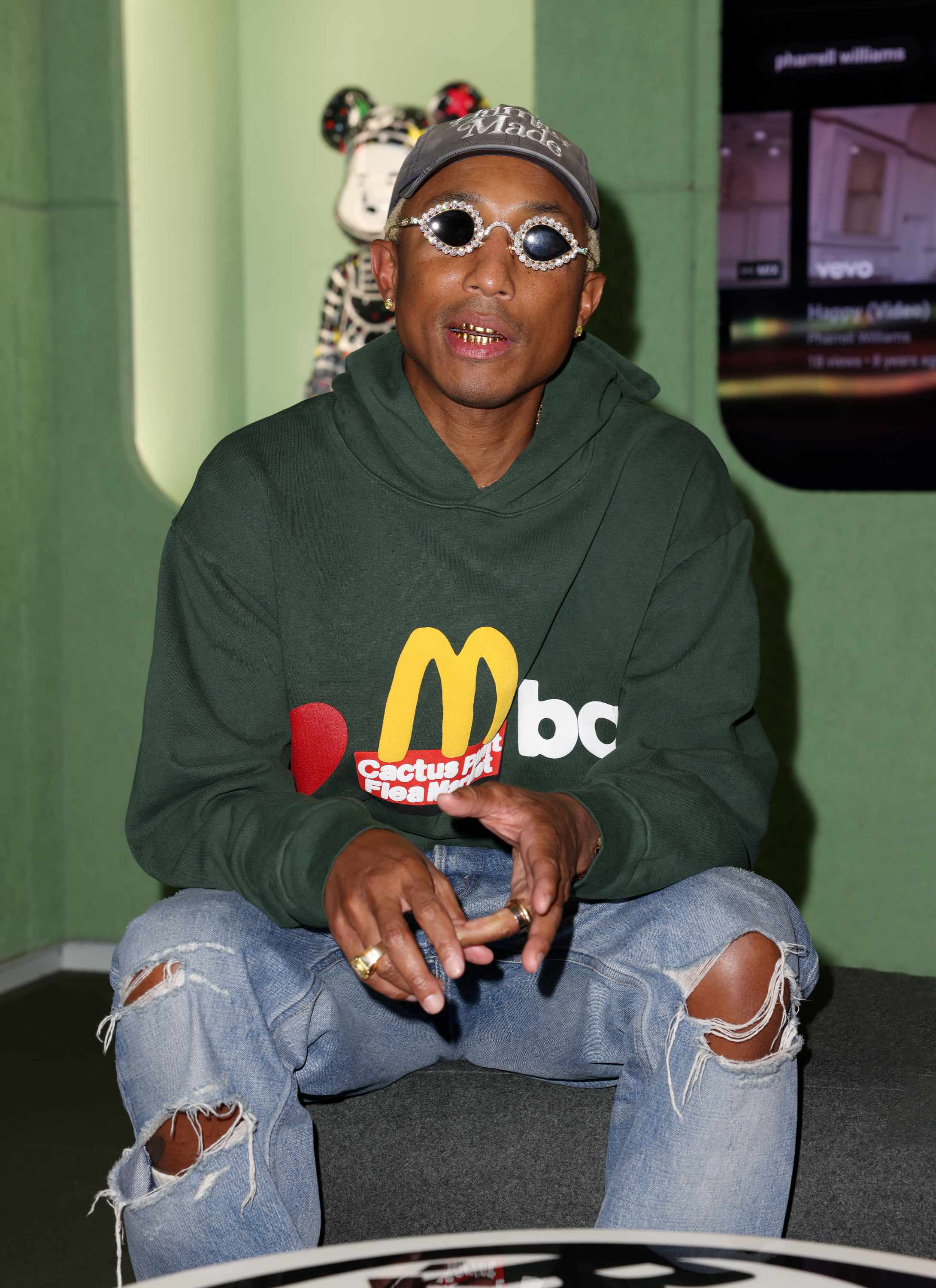Pharrell Williams wears Human Made hat, Tiffany sunglases, Cactus Plant Flea Market's McDonald's hoodie and blue jeans