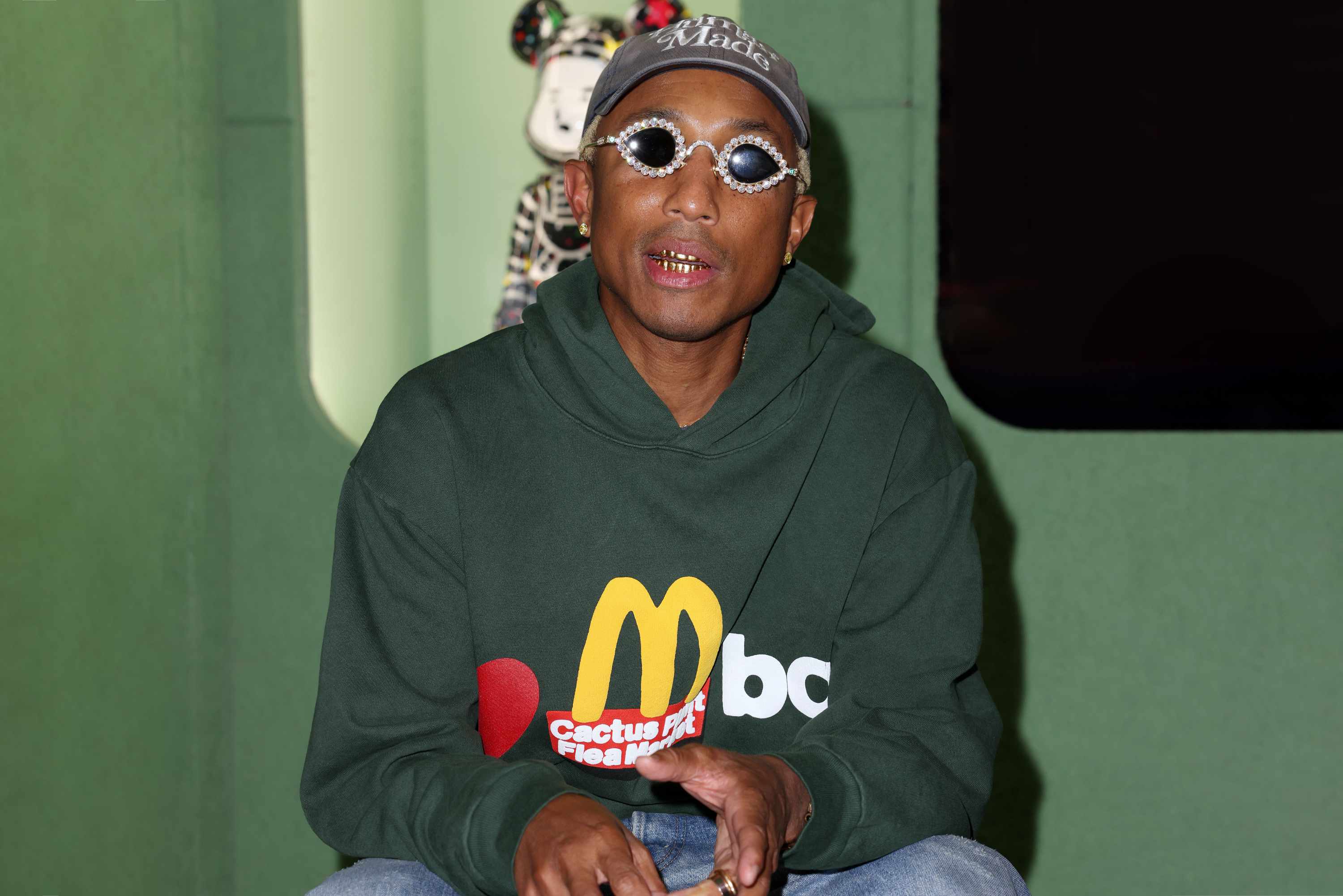 Pharrell Williams wears Human Made hat, Tiffany sunglases, Cactus Plant Flea Market's McDonald's hoodie and blue jeans