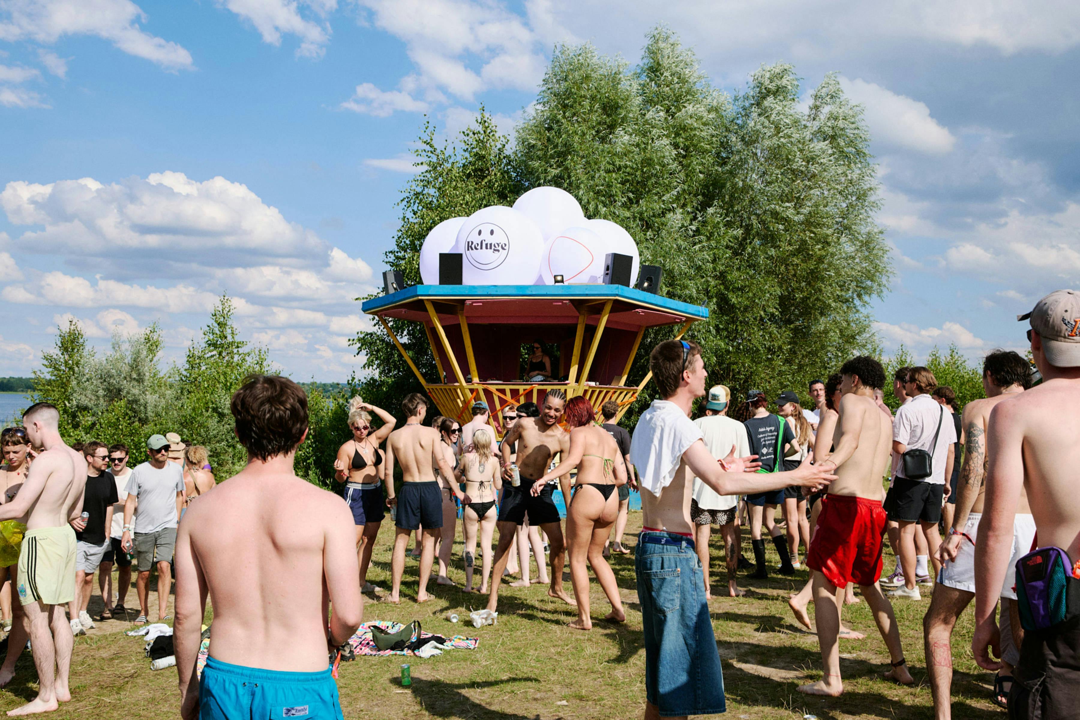 Landscape shot of people partying by a sunny lake at a festival