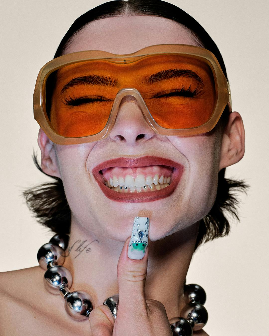 Close-up of a woman's face with a big smile, holding a finger to her mouth with Android-inspired nail art