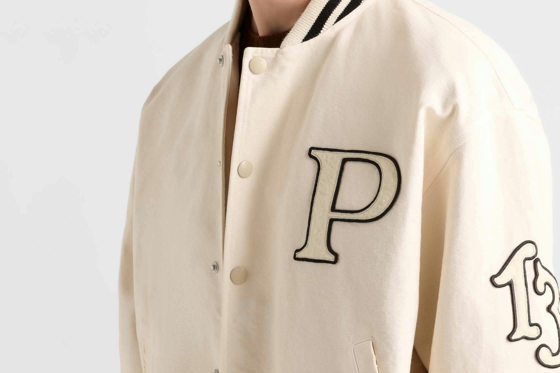 Prada's 1913 menswear capsule, including white varsity jacket, black bomber and knit cardigan