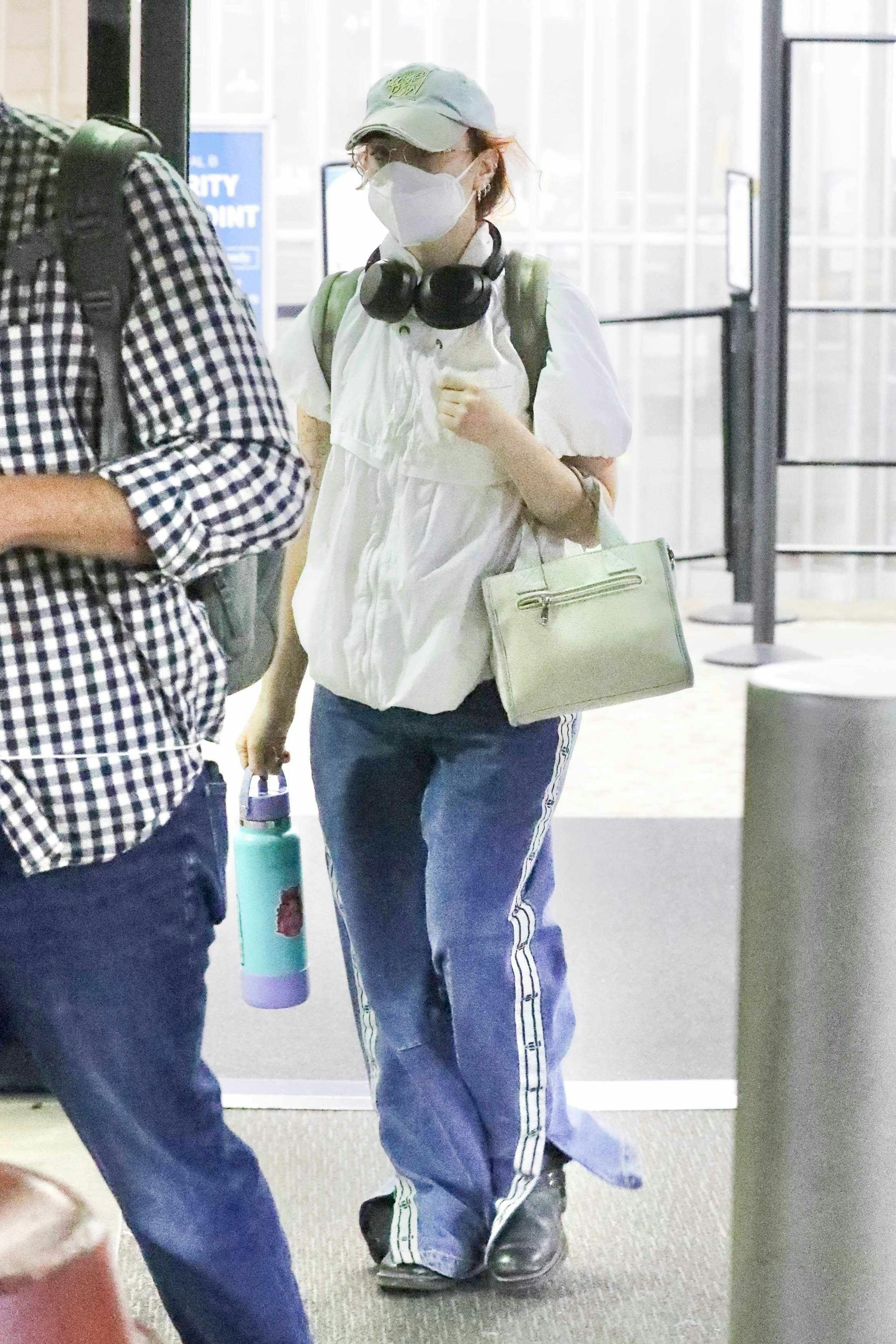 Chappell roan wears a white hat, face mask, black headphones, white shirt, tearaway denim pants and black leather biker boots