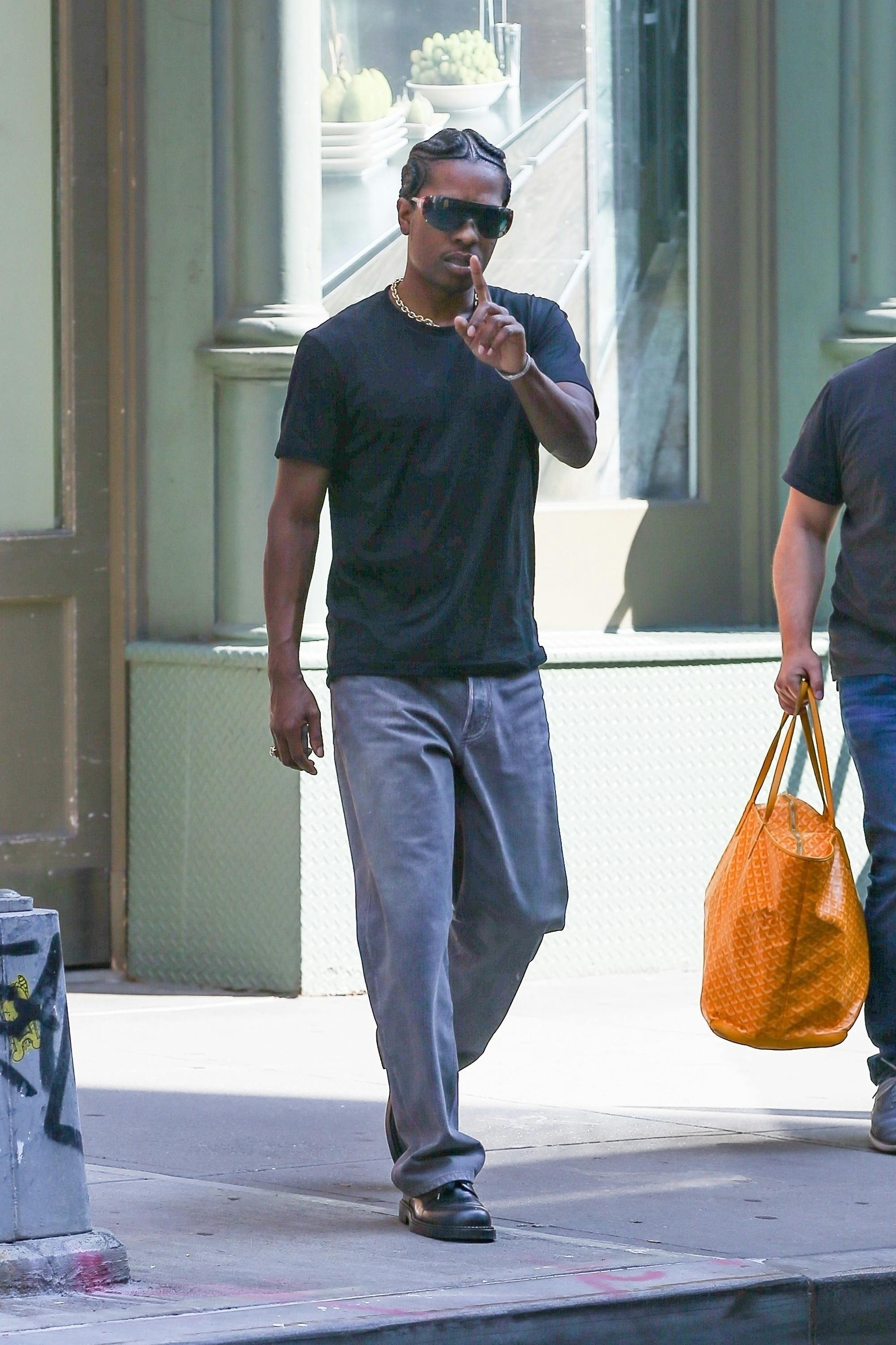 A$AP Rocky wears shield sunglasses, a black T-shirt, blue jeans and black leather shoes in New York on July 31