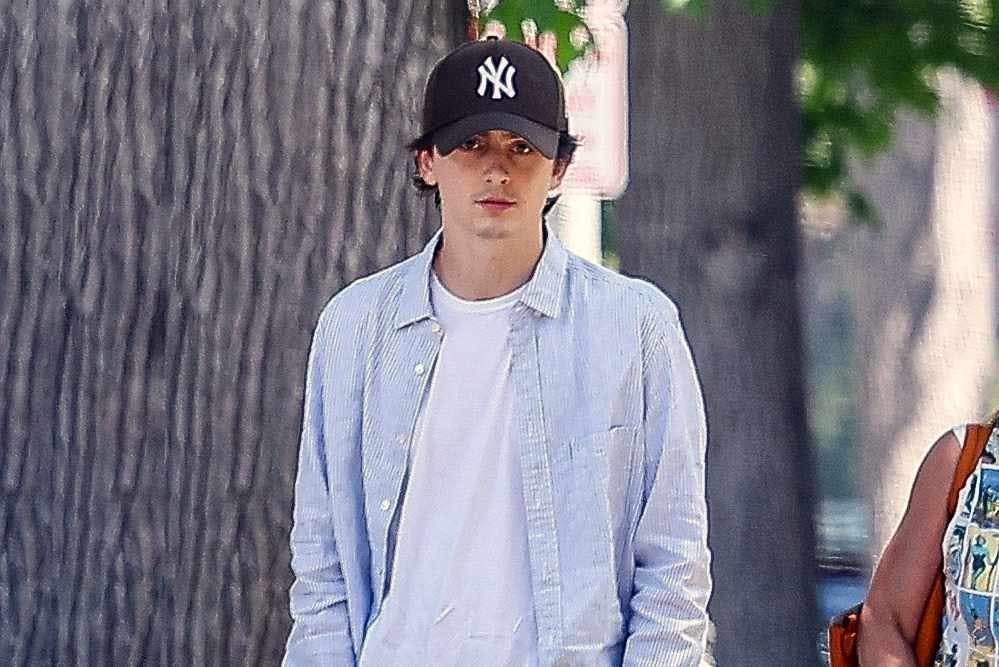 Timothee Chalamet wears a blue shirt, white T-shirt, brown yankees hat, beige shorts and white nike air force 1 sneakers while out in los angeles with his mother