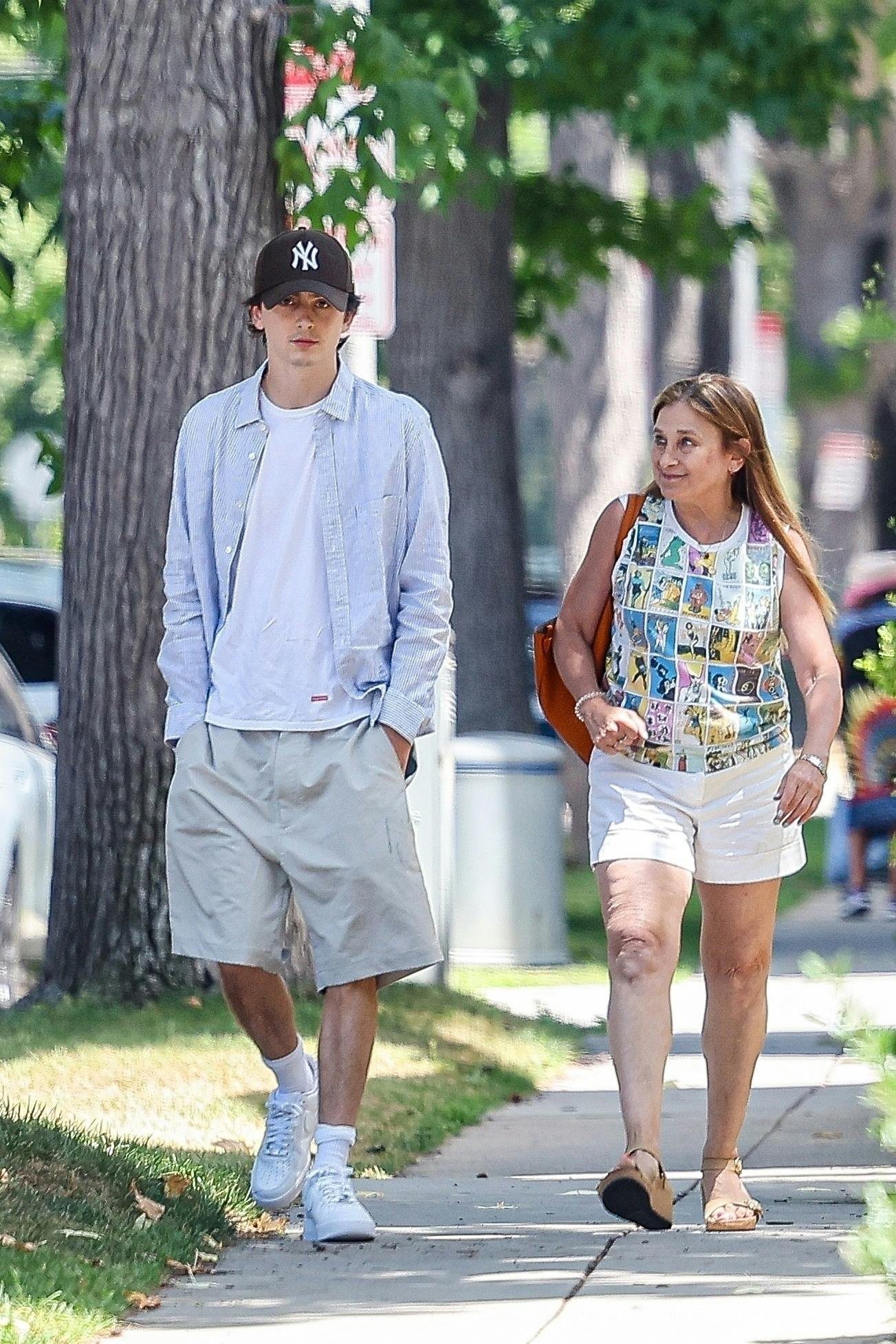 Timothee Chalamet wears a blue shirt, white T-shirt, brown yankees hat, beige shorts and white nike air force 1 sneakers while out in los angeles with his mother