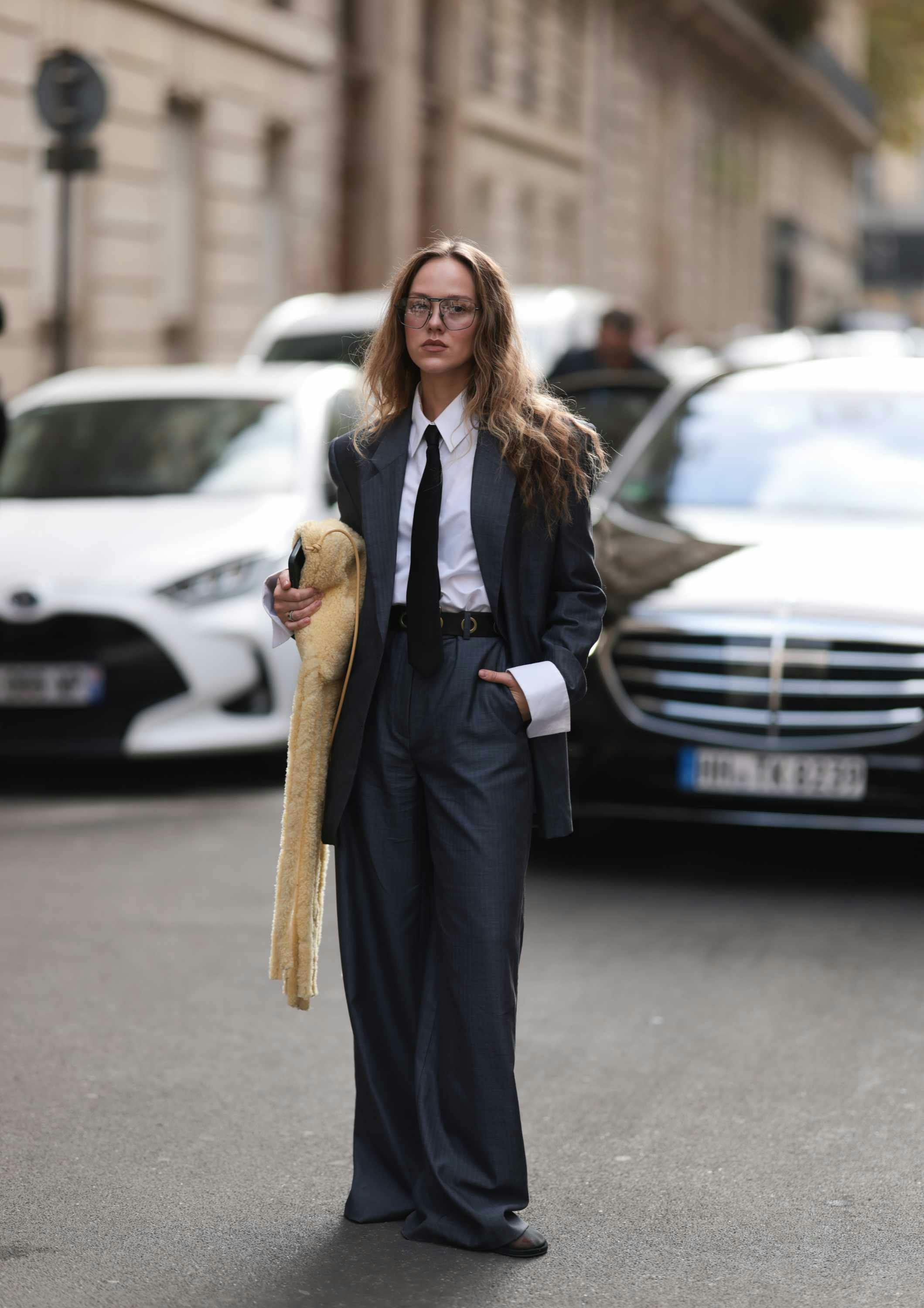 fashion week guest wears suit tie and glasses with bottega veneta parrot bag