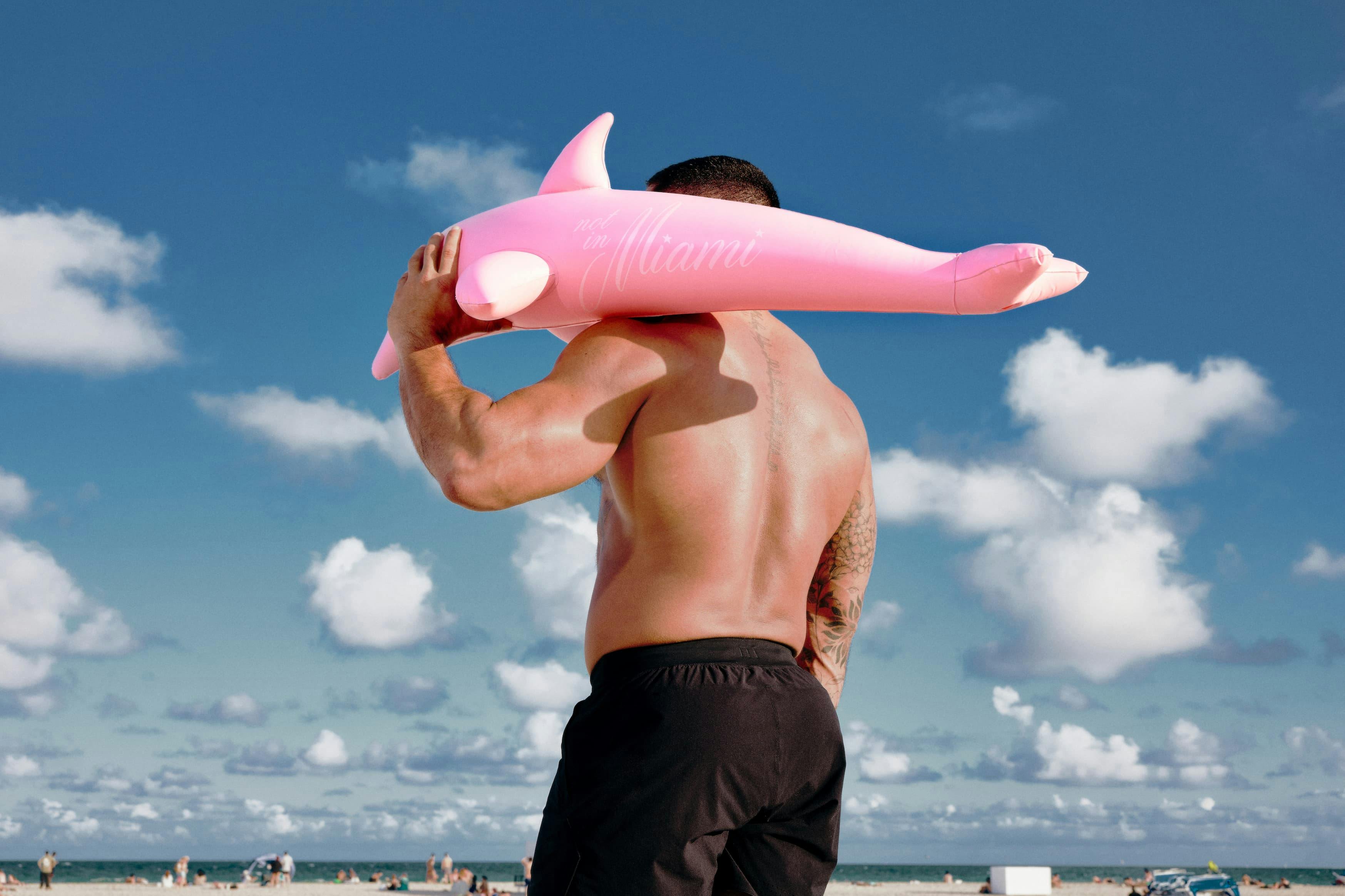 man at beach holding inflatable pink dolphin