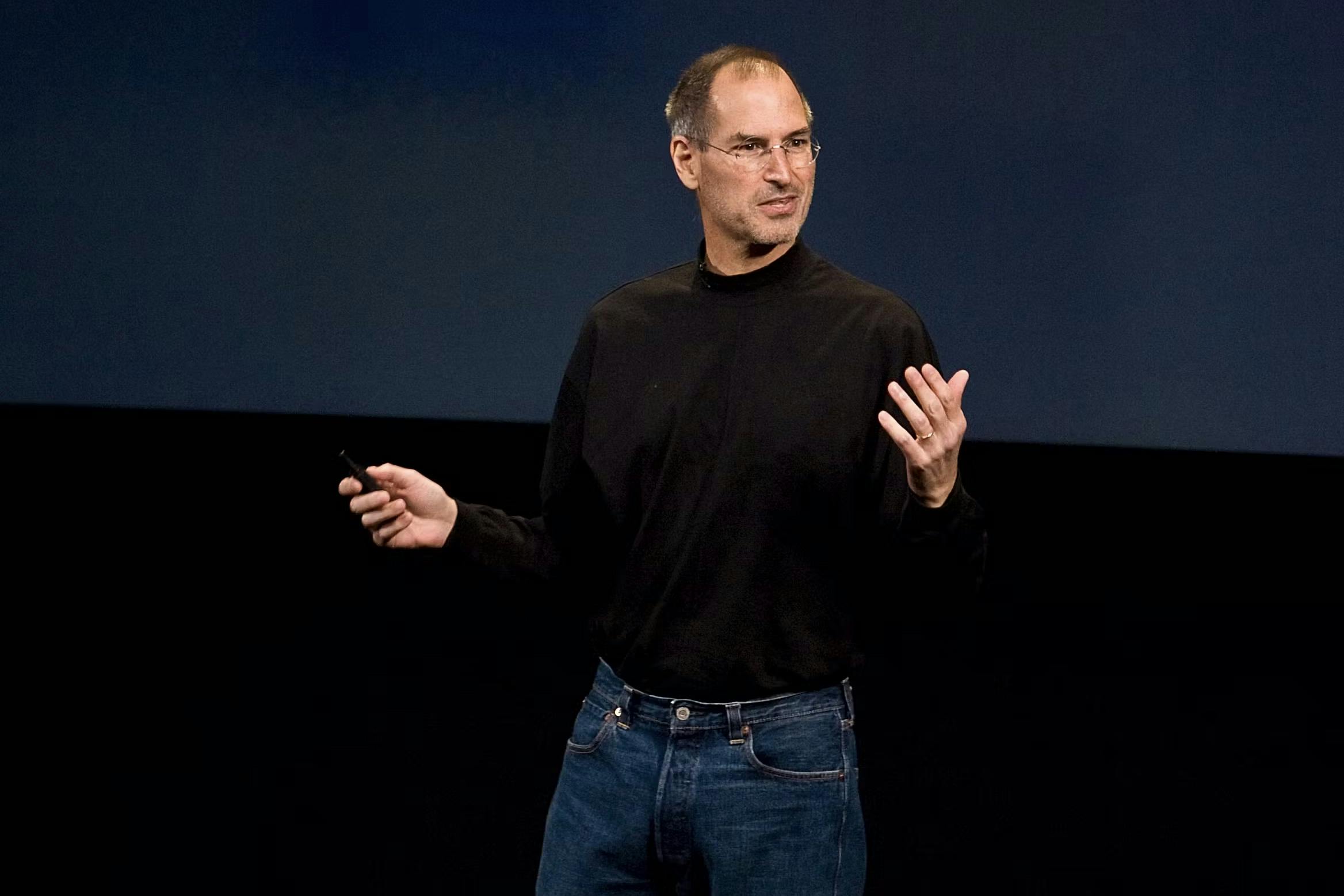 steve jobs at an apple presentation wearing a black turtleneck and blue levis jeans