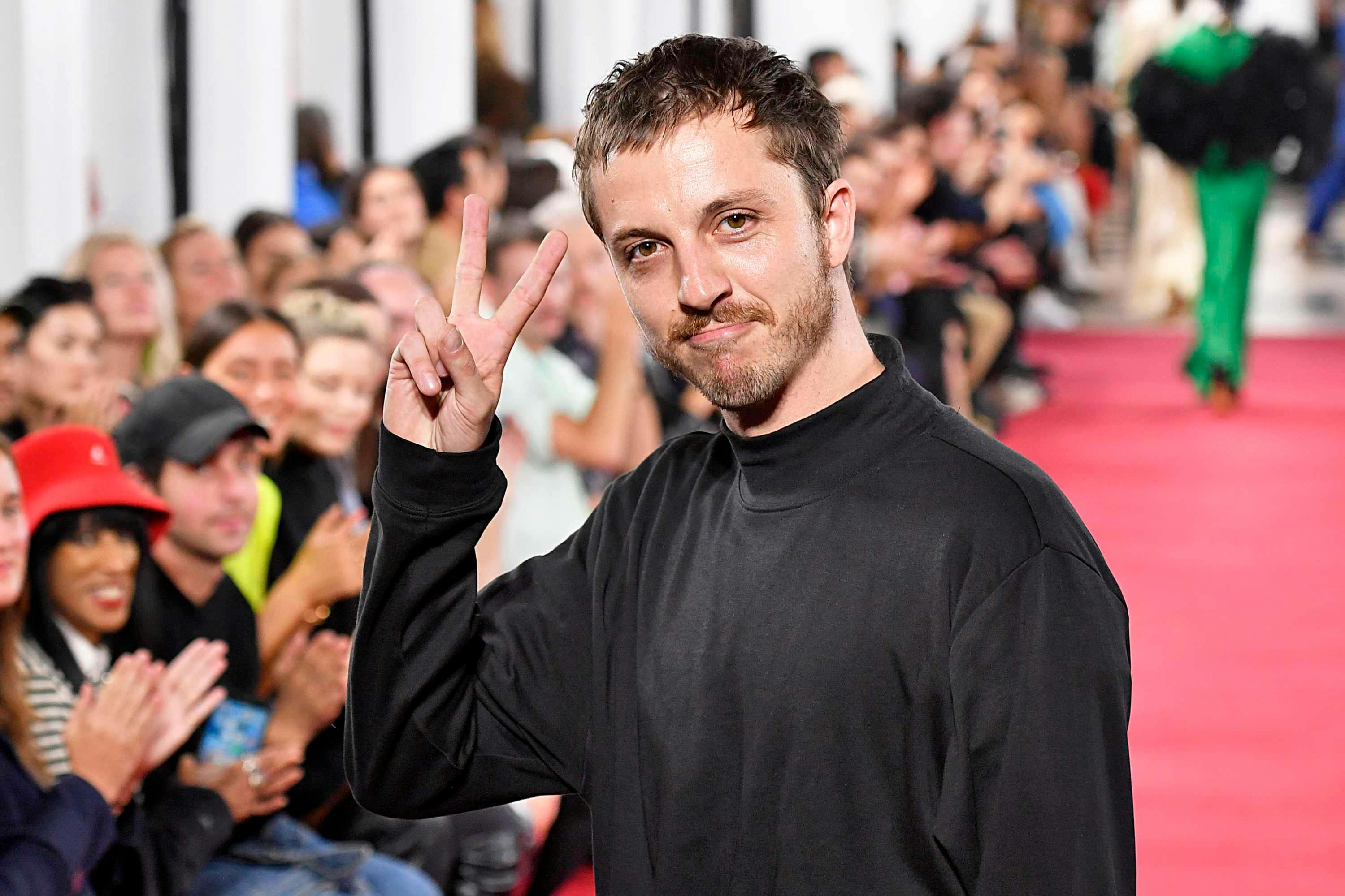 glenn martens poses with a peace sign on a runway