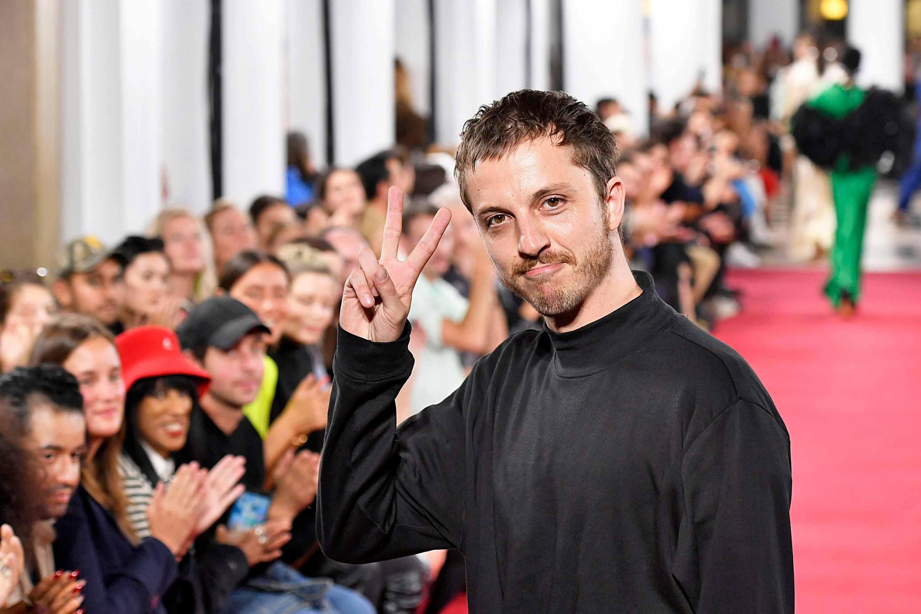 glenn martens poses with a peace sign on a runway